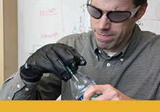 A thumbnail image of a person in lab glasses and wearing a lab glove opening a container